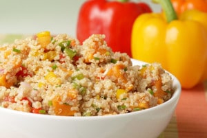 A colorful salad of quinoa, bell peppers, potato and other vegetables with red, orange and yellow bell peppers in the background